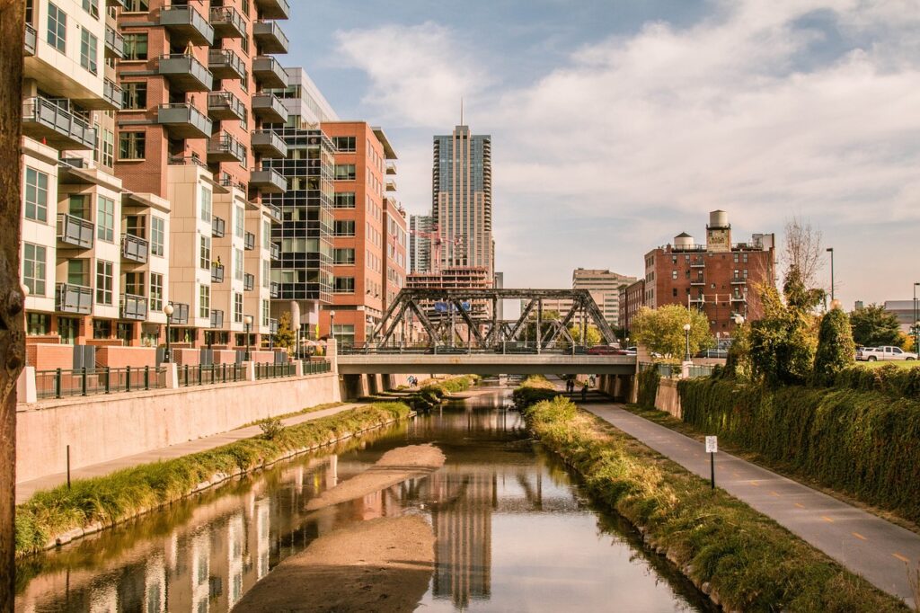 Apartment buildings beside a creek path in Denver, with downtown towers behind